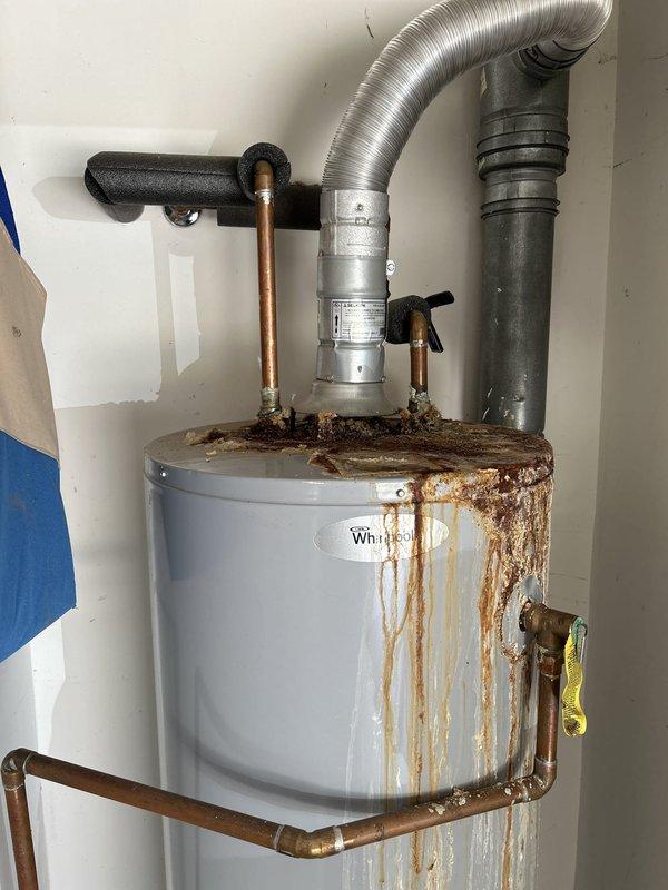 Completed plumbing estimate for 50-gallon gas water heater replacement in garage. The existing Whirlpool tank-style water heater exhibited extensive rust staining and corrosion throughout the exterior surfaces, with significant deterioration visible at top pipe connections indicating active or previous water leakage. Documented current unit condition showing rust streaks cascading vertically down the tank from compromised fittings, corroded copper piping connections, and moisture damage patterns suggesting the unit has reached end of service life and requires replacement.