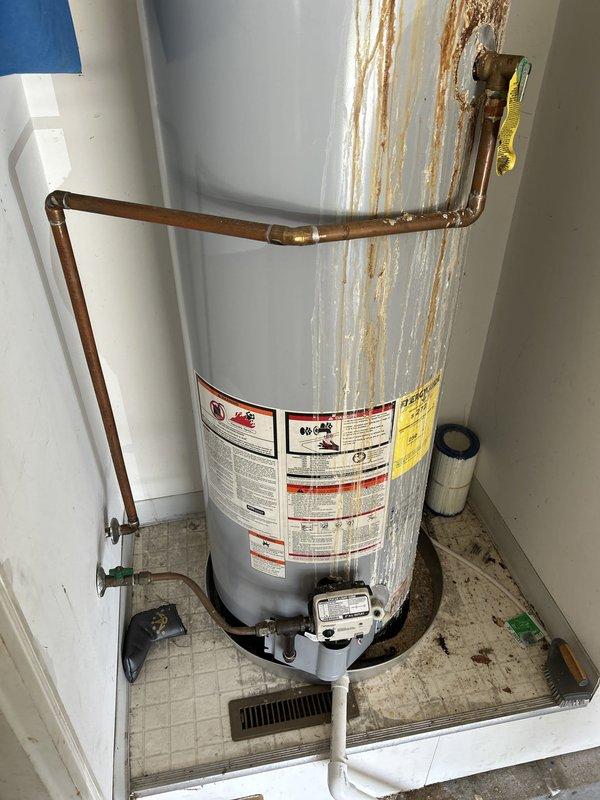 Completed plumbing estimate for 50-gallon gas water heater replacement in garage. The existing Whirlpool tank-style water heater exhibited extensive rust staining and corrosion throughout the exterior surfaces, with significant deterioration visible at top pipe connections indicating active or previous water leakage. Documented current unit condition showing rust streaks cascading vertically down the tank from compromised fittings, corroded copper piping connections, and moisture damage patterns suggesting the unit has reached end of service life and requires replacement.