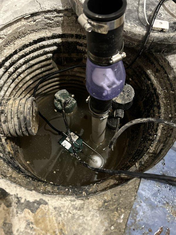 Removed failed sump pump assembly from existing concrete sump pit and installed new replacement unit with purple translucent discharge chamber and PVC piping components. Verified proper electrical connections, tested pump operation, and confirmed adequate drainage function in basement mechanical room.