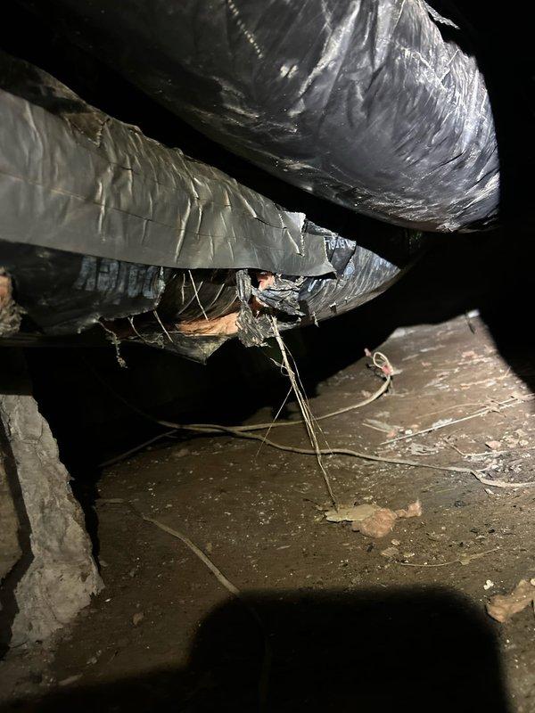 Responded to no cooling complaint on 10+ year old electric AC system with front of house unable to reach setpoint of 72°F, climbing to 79°F. Upon inspection of crawl space where indoor unit is located, found extensive deterioration of flexible ductwork insulation with multiple tears and exposed sections throughout the supply duct runs. Insulation vapor barrier had separated and was hanging loose in several areas, compromising thermal efficiency and allowing significant temperature gain in conditioned air before reaching living spaces. Observed wooden support framing beneath damaged ductwork and noted accumulated debris on crawl space floor surfaces. Located condensate removal equipment covered in heavy dust accumulation, indicating extended period without maintenance. Yellow flexible condensate line routing from pump assembly appeared functional but entire area showed signs of neglect. Documented compromised ductwork condition and explained how deteriorated insulation and potential air