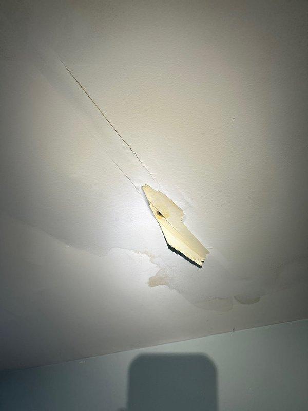 Responded to callback for water leak in second-floor bedroom originating from newly installed upstairs HVAC unit. Upon arrival, inspected ceiling damage showing diagonal crack with water staining and discoloration. Accessed attic space above affected area and located source of leak at condensate drain line. Found improperly secured PVC drain connection at air handler, allowing water to overflow onto insulation and ceiling joists. Corrected drain line installation, secured all connections, and verified proper pitch for drainage. Tested condensate system under full operation to confirm leak resolution. Documented ceiling damage with photos for repair coordination. System now operating properly with no active leaks detected.
