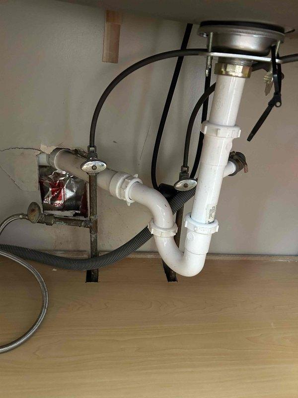 Responded to water leak behind kitchen sink and dishwasher in 1958-built home that had been active for approximately one week. Located source of leak in concealed piping behind wall cavity. Cut ceiling access panel to expose and repair compromised pipe section. Installed new PVC drain assembly under sink, securing all connections with proper clamps and fittings. Verified P-trap configuration and tested all drain lines and water supply connections for proper operation and seal integrity.