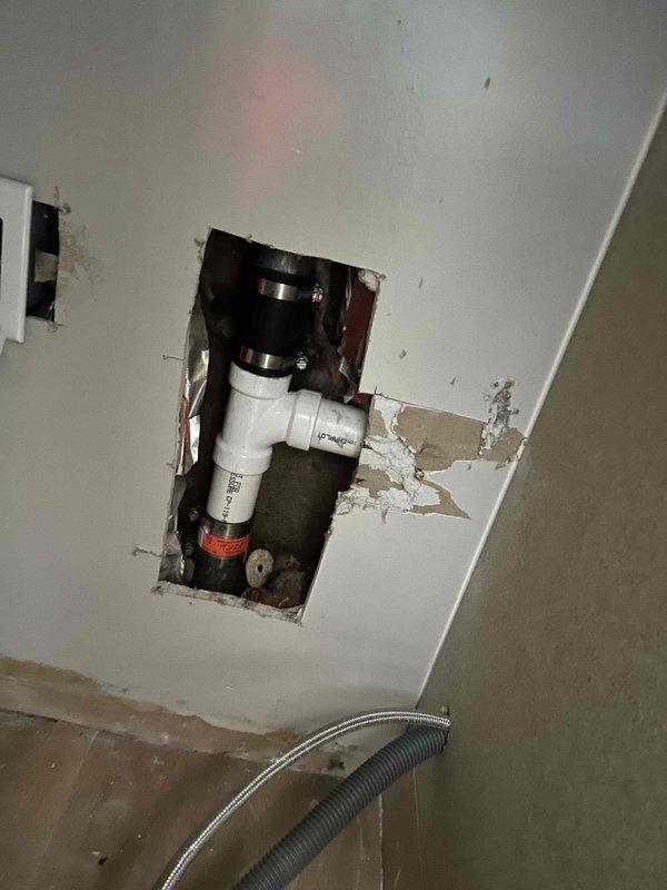 Responded to water leak behind kitchen sink and dishwasher in 1958-built home that had been active for approximately one week. Located source of leak in concealed piping behind wall cavity. Cut ceiling access panel to expose and repair compromised pipe section. Installed new PVC drain assembly under sink, securing all connections with proper clamps and fittings. Verified P-trap configuration and tested all drain lines and water supply connections for proper operation and seal integrity.