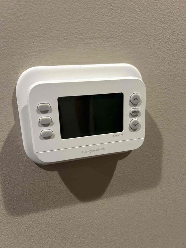 Responded to no cooling call on 1-year-old AC system with blank thermostat display. Upon arrival, found Honeywell Home digital thermostat completely unresponsive with no power to display. Traced wiring from thermostat to outdoor condensing unit and discovered failed dual-run capacitor (TRCED455, 45/5 MFD, 440VAC) with visible corrosion and debris accumulation at terminals. Replaced defective capacitor with new OEM-equivalent unit, cleaned terminal connections, and verified proper wire connections. Restored power to thermostat, confirmed display functionality, and tested system operation through complete cooling cycle. System now operating within normal parameters with proper thermostat communication and control.