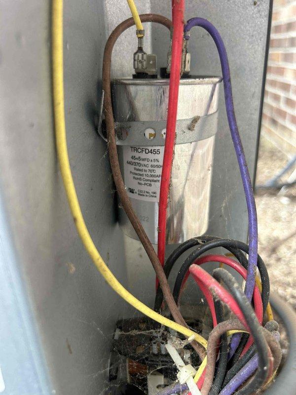 Responded to no cooling call on 1-year-old AC system with blank thermostat display. Upon arrival, found Honeywell Home digital thermostat completely unresponsive with no power to display. Traced wiring from thermostat to outdoor condensing unit and discovered failed dual-run capacitor (TRCED455, 45/5 MFD, 440VAC) with visible corrosion and debris accumulation at terminals. Replaced defective capacitor with new OEM-equivalent unit, cleaned terminal connections, and verified proper wire connections. Restored power to thermostat, confirmed display functionality, and tested system operation through complete cooling cycle. System now operating within normal parameters with proper thermostat communication and control.
