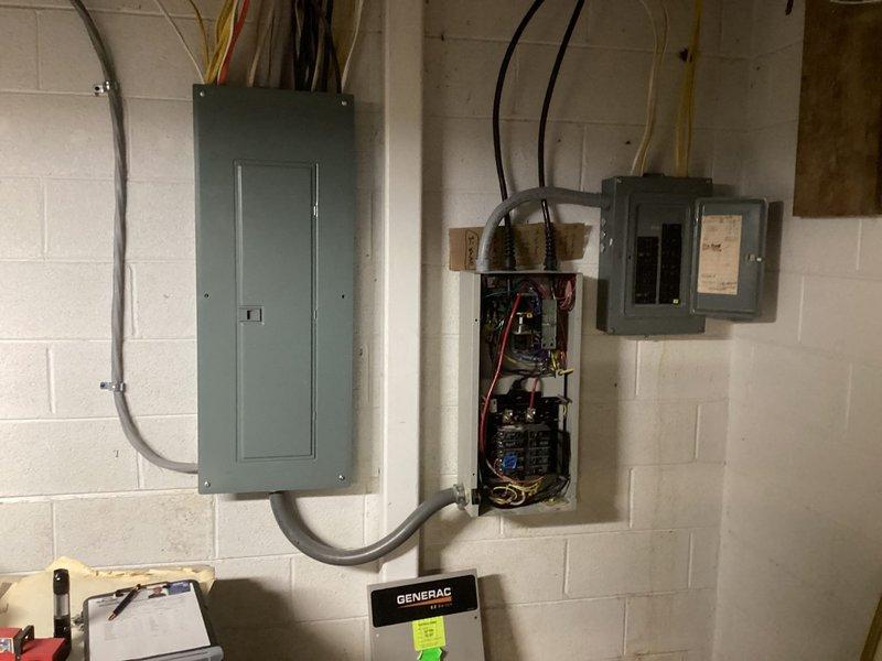 Conducted comprehensive electrical assessment for standby generator installation. Evaluated existing electrical infrastructure including main service panel, transfer switch location, and routing pathways for generator feeders. Documented current electrical configuration with Generac equipment already present, noting existing conduit runs, wire terminations, and panel connections. Assessed exterior utility routing where PVC conduit and flexible conduit converge at building corner, observing moisture conditions that may impact installation planning. Photographed open electrical panels revealing multi-conductor feeders, bus bar connections, and existing generator interface components to provide accurate material and labor estimates for completing the generator electrical integration.
