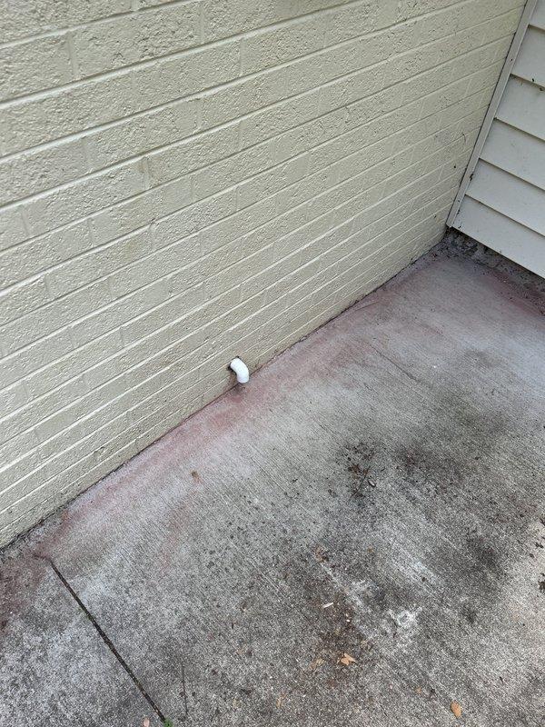 Completed repiping of drain pan discharge line to exterior of building. Installed new PVC drain line from air handler drain pan, routing through wall to terminate outside. Drain outlet now properly discharges condensate to exterior concrete pad, preventing indoor water damage. Verified proper drainage flow and secure pipe connections at both interior pan connection and exterior wall penetration.