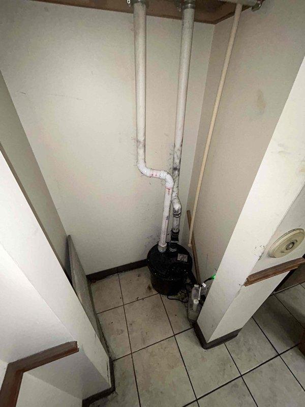 Removed and replaced existing sump pump system in utility room. Installed new black cylindrical sump pump unit at base of white PVC drainage piping configuration, ensuring proper connections to vertical discharge lines and establishing reliable water removal capability for the space.