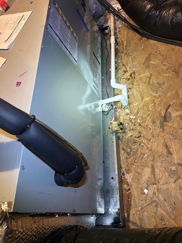 Responded to water leak complaint at attic-mounted electric heat pump air handler system. Upon arrival, observed water damage at ceiling return air grille with visible staining and discoloration indicating prolonged moisture exposure during customer's absence. Inspected air handler unit and surrounding area, documenting conditions with photographs. Found condensate drain system with PVC drain line and brass valve assembly. Investigated source of water intrusion to determine cause of overflow condition. System evaluated for proper drainage function and potential blockages that may have caused backup during extended unattended operation period.