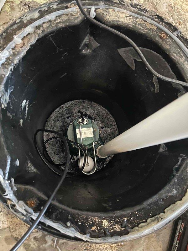Responded to service call for non-functioning sump pump in basement of 60-year-old residence. Upon arrival, found sump pump improperly draining into sewer line, causing overflow conditions when washing machine discharged. Issue had persisted for approximately five days prior to service call.

Performed thorough inspection of existing sump pump system and basin. Identified improper drainage configuration as primary cause of overflow issues. Sump basin showed significant age-related deterioration with heavy staining and buildup on interior walls. Existing pump equipment was assessed for operational status and proper installation requirements.

Installed new sump pump system with appropriate discharge piping. Configured white PVC discharge line with vertical run from pump basin. Installed electronic monitoring device with sensor on discharge pipe to provide system status indication and alert capability. Secured monitoring equipment to discharge pipe using cable straps and connected power 