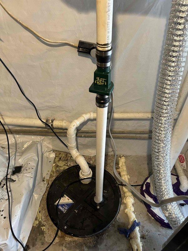 Responded to service call for non-functioning sump pump in basement of 60-year-old residence. Upon arrival, found sump pump improperly draining into sewer line, causing overflow conditions when washing machine discharged. Issue had persisted for approximately five days prior to service call.

Performed thorough inspection of existing sump pump system and basin. Identified improper drainage configuration as primary cause of overflow issues. Sump basin showed significant age-related deterioration with heavy staining and buildup on interior walls. Existing pump equipment was assessed for operational status and proper installation requirements.

Installed new sump pump system with appropriate discharge piping. Configured white PVC discharge line with vertical run from pump basin. Installed electronic monitoring device with sensor on discharge pipe to provide system status indication and alert capability. Secured monitoring equipment to discharge pipe using cable straps and connected power 