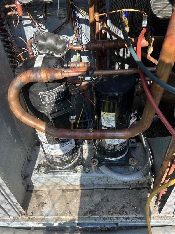 Performed comprehensive leak search on Bryant commercial package unit utilizing ultrasonic leak detection equipment. Inspection revealed significant refrigerant leak at compressor discharge line connection, evidenced by heavy oil accumulation and severe corrosion at copper piping joint between dual compressor system. The U-bend copper discharge line exhibited advanced oxidation and deterioration at the connection point, with black viscous oil residue indicating active refrigerant leak. Documented findings with photographic evidence showing compromised piping integrity and recommended repair options for management review.