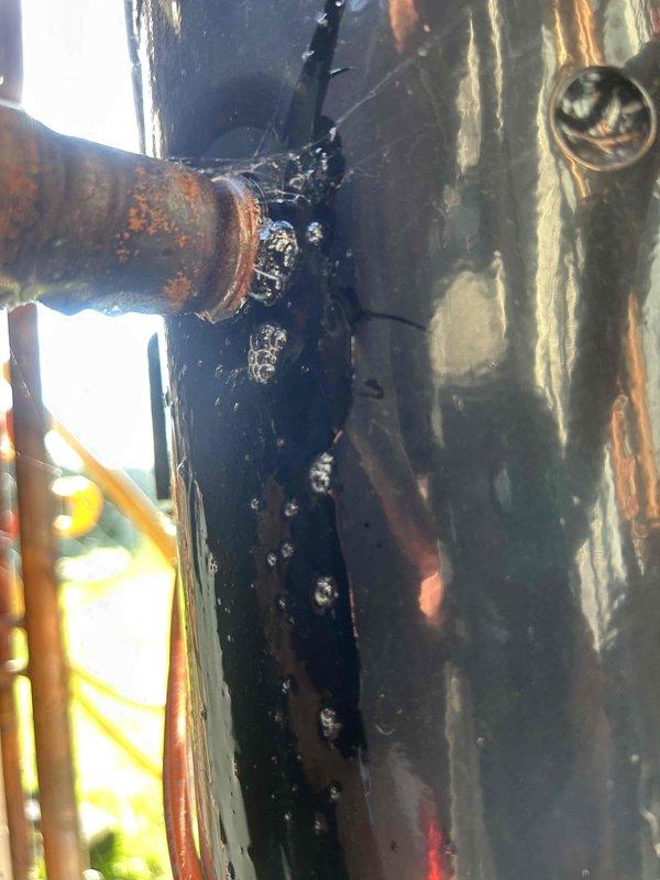 Performed comprehensive leak search on Bryant commercial package unit utilizing ultrasonic leak detection equipment. Inspection revealed significant refrigerant leak at compressor discharge line connection, evidenced by heavy oil accumulation and severe corrosion at copper piping joint between dual compressor system. The U-bend copper discharge line exhibited advanced oxidation and deterioration at the connection point, with black viscous oil residue indicating active refrigerant leak. Documented findings with photographic evidence showing compromised piping integrity and recommended repair options for management review.