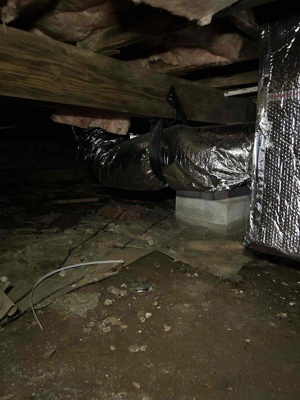 Technician performed warranty service inspection in attic space to assess HVAC system installation and ductwork condition. Upon inspection, identified need for warranty mitigation sensor installation, which will be completed during scheduled return visit pending tenant availability confirmation. Documented existing flexible ductwork installation with metallic ducting and reflective foil-faced insulation materials, noting proper support structure and insulation placement between roof joists. Captured photographic documentation of attic space conditions, including exposed wooden beams, pink fiberglass insulation between rafters, and OSB flooring with HVAC ductwork properly secured with black straps to structural beams.
