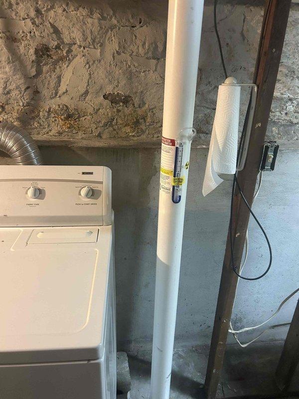 Conducted on-site assessment of basement laundry area to provide estimate for relocating dryer vent. Evaluated existing utility infrastructure including plumbing lines, electrical conduits, and current laundry equipment configuration to determine optimal routing path for dryer exhaust. Documented existing conditions with photos showing washing machine placement, PVC drainage system, water filtration equipment, exposed ceiling joists, and concrete block wall structure to develop relocation plan and material requirements for future dryer vent installation.