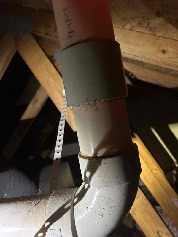 Responded to report of pipe leaking in attic during rainfall, initially identified by HVAC contractor during recent installation. Upon inspection, located vertical pipe system running through attic framing with visible signs of moisture intrusion and residue accumulation on PVC sections. Examined multi-segment pipe assembly consisting of copper, gray, and white PVC components joined with metal bands and secured with perforated metal hangers. Documented extensive discoloration and debris buildup around pipe joints, indicating prolonged exposure to water and potential leak points. Photographed affected areas showing yellowed residue and grime accumulation on pipe surfaces. Assessed structural framing and surrounding areas for water damage. Provided diagnostic findings and recommendations for repair.