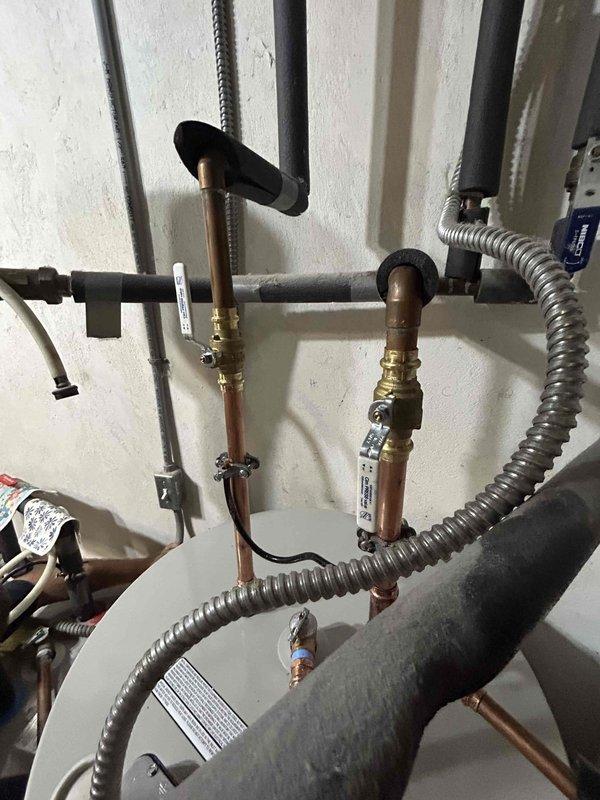 Removed and hauled away existing 80-gallon electric water heater and replaced with new unit supplied by contractor. Installed recirculation pump system with copper piping, brass isolation valves with T-handle shutoff, and black foam pipe insulation on hot water lines. Configured plumbing assembly with multiple brass fittings, elbows, and tees, incorporating blue push-fit connectors at key connection points. Installed flexible metal conduit for electrical connections. Positioned new water heater tank on existing tile floor base in corner location. Completed all copper pipe connections at tank base with ball valve shutoff for water supply control. Pressure tested entire system, verified proper pump operation, and inspected all connections for leaks prior to departure. System confirmed functional and ready for service.