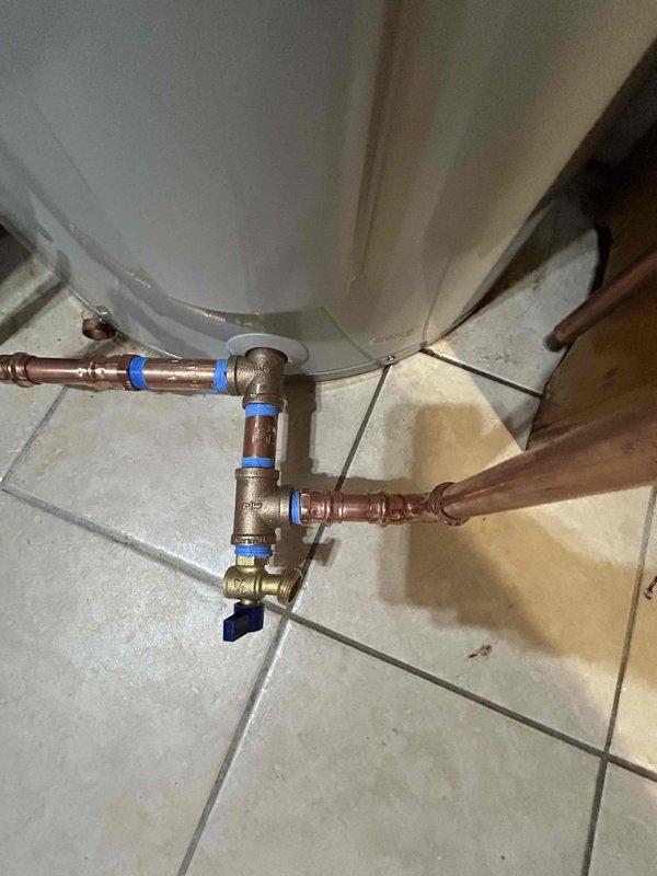 Removed and hauled away existing 80-gallon electric water heater and replaced with new unit supplied by contractor. Installed recirculation pump system with copper piping, brass isolation valves with T-handle shutoff, and black foam pipe insulation on hot water lines. Configured plumbing assembly with multiple brass fittings, elbows, and tees, incorporating blue push-fit connectors at key connection points. Installed flexible metal conduit for electrical connections. Positioned new water heater tank on existing tile floor base in corner location. Completed all copper pipe connections at tank base with ball valve shutoff for water supply control. Pressure tested entire system, verified proper pump operation, and inspected all connections for leaks prior to departure. System confirmed functional and ready for service.