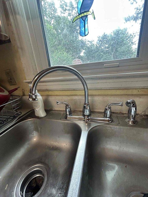Responded to service call for leak at recently installed kitchen faucet in 65-year-old residence. Upon arrival, inspected chrome dual-handle faucet with arched spout and separate spray nozzle mounted on double-basin stainless steel sink. Identified source of leak and tightened supply line connections beneath sink. Examined under-sink plumbing configuration including P-trap assembly, garbage disposal unit with corrugated drain hose, and supply valves to ensure proper sealing and connection integrity. Tested faucet operation at multiple flow rates and verified all connections remained dry under pressure. Confirmed leak was resolved and no additional plumbing issues were present in the immediate area.
