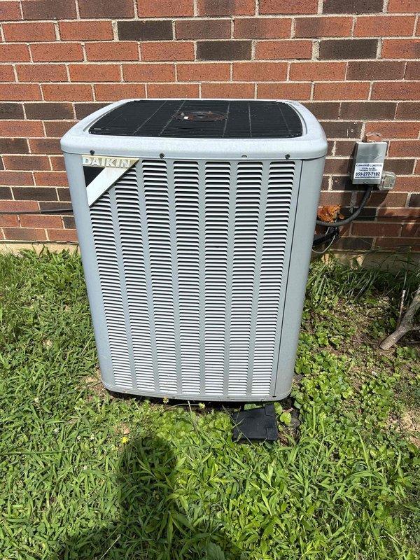 Responded to report of AC unit freezing/icing up at intake while still maintaining cooling function on an 8-year-old Daikin outdoor condensing unit. Upon arrival, performed visual inspection of the outdoor unit positioned against brick exterior, noting overall functional condition with normal weathering for age. Accessed indoor air handler to assess airflow and system performance. Measured and documented temperature readings using digital instrumentation on evaporator coil and ductwork surfaces to evaluate operating parameters. Photographed outdoor condensing unit showing proper installation on pad with electrical disconnect and refrigerant line connections visible. Documented indoor measurements and conditions within air handler compartment. Based on freezing symptoms at intake, likely causes include restricted airflow from dirty air filter, low refrigerant charge, or reduced airflow across evaporator coil requiring further diagnostic evaluation or preventive maintenance.