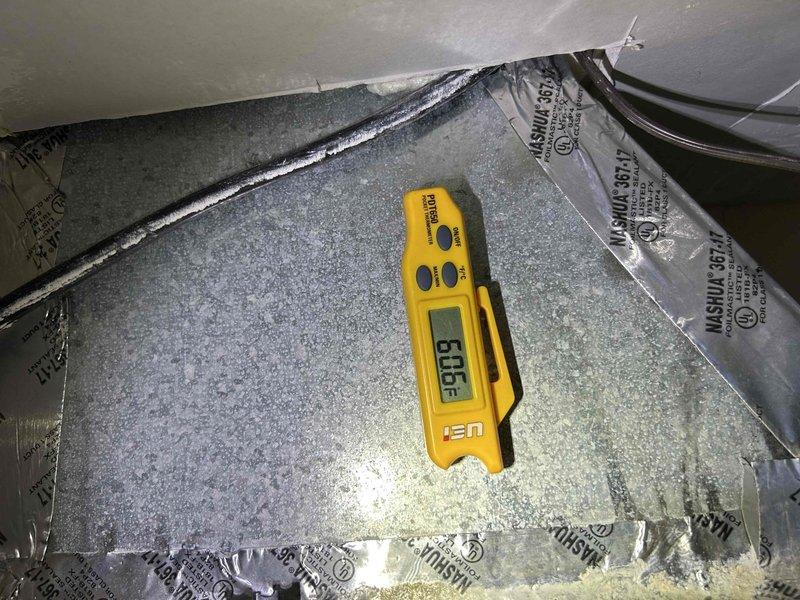Responded to report of AC unit freezing/icing up at intake while still maintaining cooling function on an 8-year-old Daikin outdoor condensing unit. Upon arrival, performed visual inspection of the outdoor unit positioned against brick exterior, noting overall functional condition with normal weathering for age. Accessed indoor air handler to assess airflow and system performance. Measured and documented temperature readings using digital instrumentation on evaporator coil and ductwork surfaces to evaluate operating parameters. Photographed outdoor condensing unit showing proper installation on pad with electrical disconnect and refrigerant line connections visible. Documented indoor measurements and conditions within air handler compartment. Based on freezing symptoms at intake, likely causes include restricted airflow from dirty air filter, low refrigerant charge, or reduced airflow across evaporator coil requiring further diagnostic evaluation or preventive maintenance.