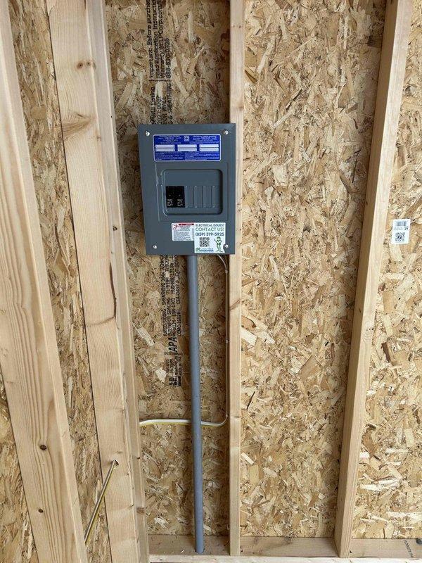 Installed 100-amp electrical panel with two circuit breakers in new construction during rough-in phase, mounted centrally between wall studs on OSB sheathing. Wired and installed electrical devices including one GFCI receptacle, two duplex receptacles, one single-pole switch, and two keyless light fixtures with bulbs. Ran conduit from panel bottom along wall with proper securing straps, and mounted outlet boxes at standard heights on wall studs throughout the unfinished space.