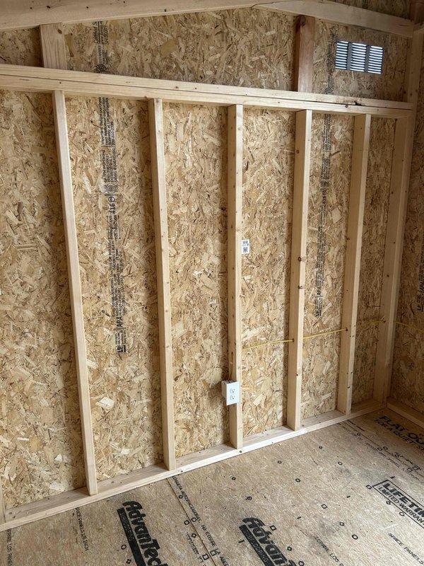Installed 100-amp electrical panel with two circuit breakers in new construction during rough-in phase, mounted centrally between wall studs on OSB sheathing. Wired and installed electrical devices including one GFCI receptacle, two duplex receptacles, one single-pole switch, and two keyless light fixtures with bulbs. Ran conduit from panel bottom along wall with proper securing straps, and mounted outlet boxes at standard heights on wall studs throughout the unfinished space.