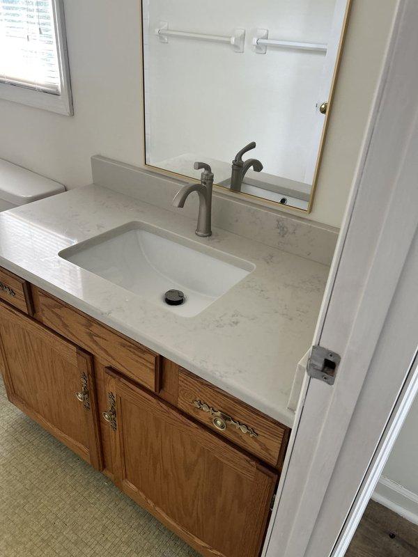 Technician successfully installed two customer-provided bathroom sink faucets in a 1980s-built home following countertop replacement. Installation included mounting single-handle brushed nickel faucets to new white quartz countertops with undermount sinks, connecting hot and cold water supply lines with flexible hoses, and installing drain assemblies with P-trap configurations. Both faucet installations were tested for proper operation and checked for leaks, with all connections secured and functioning correctly.