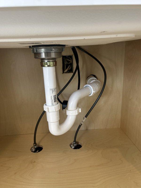 Reconnected kitchen sink plumbing assembly that had been previously disconnected. Installed P-trap configuration with chrome tailpiece and white PVC drain lines, ensuring proper alignment and secure connections to wall drain. Verified all fittings were leak-free and drain flow was functioning correctly.