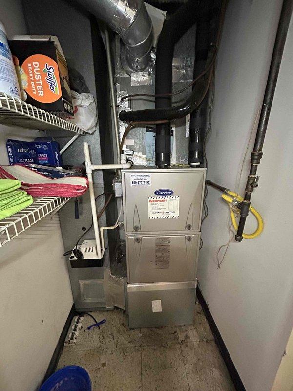 Responded to water leak complaint at indoor HVAC unit in utility room that began the previous night. Upon inspection, found condensate pump system with drain pan positioned beneath Carrier furnace air handler showing signs of moisture accumulation on metallic surfaces. Documented existing condensate management setup including white plastic condensate pump unit on black drain pan with connected PVC drainage piping and verified electrical connections to wall outlet.