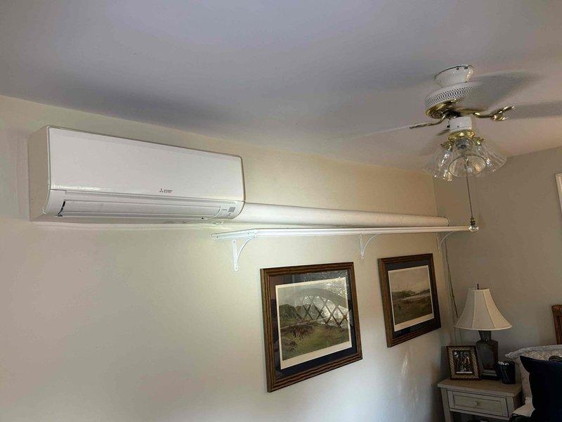 Responded to no cooling complaint on 3-year-old Mitsubishi Electric ductless mini-split system located in upstairs bedroom. Upon arrival, confirmed indoor unit was not cooling and observed greenish-yellow liquid discharge running down interior wall below unit. Visual inspection revealed significant condensate leakage from evaporator coil area with moisture staining on wall surface and evidence of biological growth in drain system. Diagnosed clogged condensate drain line causing water backup and overflow from drain pan. Cleared blockage from condensate drain line, flushed system with appropriate cleaning solution to remove algae buildup, and verified proper drainage. Tested unit operation to confirm cooling function restored and condensate properly draining without leakage. Recommended monitoring system and scheduling preventive maintenance to prevent future drain line blockages.