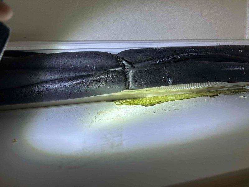 Responded to no cooling complaint on 3-year-old Mitsubishi Electric ductless mini-split system located in upstairs bedroom. Upon arrival, confirmed indoor unit was not cooling and observed greenish-yellow liquid discharge running down interior wall below unit. Visual inspection revealed significant condensate leakage from evaporator coil area with moisture staining on wall surface and evidence of biological growth in drain system. Diagnosed clogged condensate drain line causing water backup and overflow from drain pan. Cleared blockage from condensate drain line, flushed system with appropriate cleaning solution to remove algae buildup, and verified proper drainage. Tested unit operation to confirm cooling function restored and condensate properly draining without leakage. Recommended monitoring system and scheduling preventive maintenance to prevent future drain line blockages.