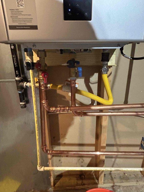 Removed existing tank-style water heater and installed customer-supplied Rinnai tankless water heater unit. Ran necessary gas piping including flexible yellow gas line connections to accommodate the new tankless system requirements. Installed copper water supply lines with shut-off valves (red and blue handled) and completed all plumbing connections to the unit. Mounted unit securely to wall framing and connected electrical wiring. Configured digital display and verified proper operation showing temperature reading of 105 degrees. Note: Tech to return for follow-up visit to install comfort valve and activate built-in recirculating pump for hot water recirculation system.
