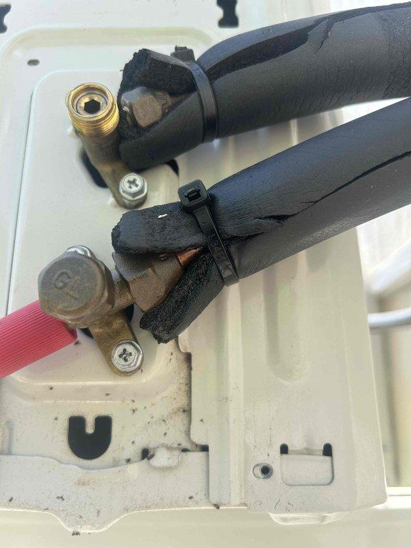 Responded to callback for minisplit installation experiencing error code indicating potential refrigerant leak or airflow restriction. Upon inspection, examined refrigerant line set connections at service valve assembly and documented condition of insulated copper lines, brass fittings, and mounting hardware. Both suction and liquid line connections showed proper mechanical assembly with compression fittings secured by zip ties, though insulation exhibited minor wear at connection points and equipment panel displayed dust accumulation, suggesting the issue may be related to airflow restriction rather than refrigerant leakage at the visible service ports.