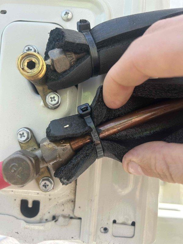 Responded to callback for minisplit installation experiencing error code indicating potential refrigerant leak or airflow restriction. Upon inspection, examined refrigerant line set connections at service valve assembly and documented condition of insulated copper lines, brass fittings, and mounting hardware. Both suction and liquid line connections showed proper mechanical assembly with compression fittings secured by zip ties, though insulation exhibited minor wear at connection points and equipment panel displayed dust accumulation, suggesting the issue may be related to airflow restriction rather than refrigerant leakage at the visible service ports.