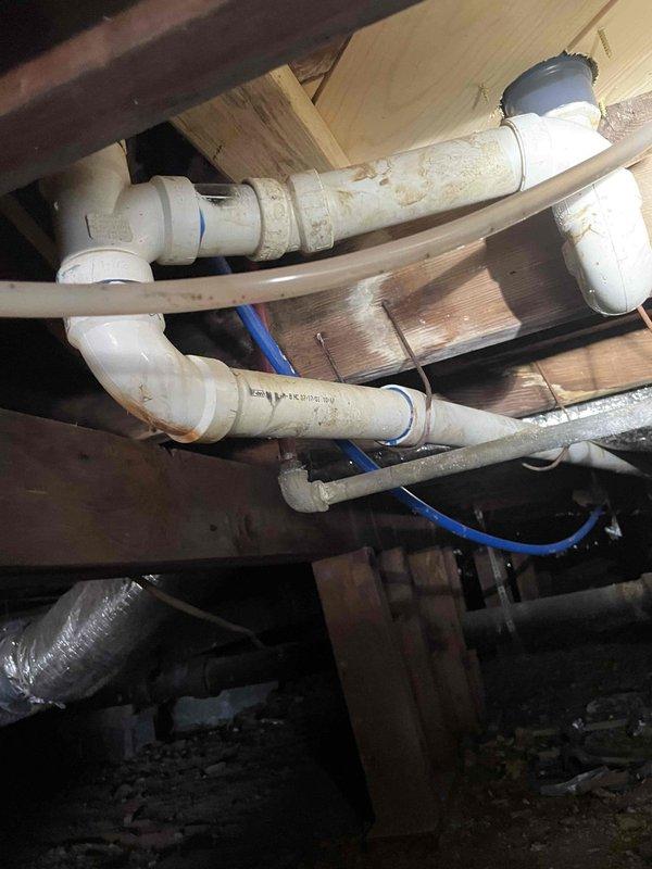Responded to kitchen sink line backup at 68-year-old residence. Previous snaking attempt by homeowner had reached approximately 25 feet without clearing the obstruction. Upon arrival, assessed the existing plumbing configuration in the crawl space, which consisted of white PVC drainage pipes with multiple elbows and connections showing age-related discoloration. Determined that blockage was located beyond the initial 25-foot reach. Utilized extended cable equipment to access and clear the clog in the main drain line. Successfully restored proper drainage flow to the kitchen sink. Inspected all visible pipe connections and joints in the crawl space for leaks or damage during the clearing process. Verified complete water flow and drainage functionality upon completion.