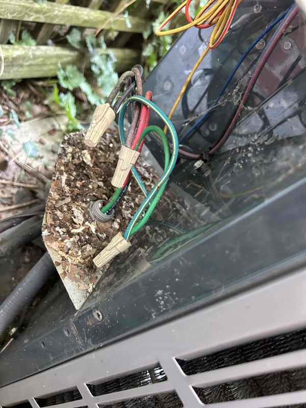 Responded to no cooling complaint on upstairs electric air conditioning system. Upon inspection, found outdoor condenser unit inoperative due to severely deteriorated electrical connection point with extensive wood rot and weather damage at the disconnect block. The compromised mounting and wiring posed both operational failure and safety concerns. Multiple colored conductors showed exposure to elements with significant decay of the wooden electrical junction box. Documented conditions of both outdoor condensing units positioned on concrete pad, noting advanced age of equipment and environmental exposure. System requires electrical repairs and replacement of damaged disconnect components to restore safe operation.
