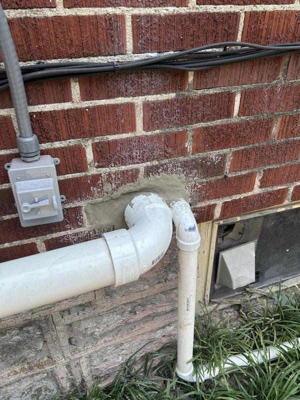Removed existing discharge and vent piping configuration and rerouted lines through the bandboard in the basement. Cut out old PVC sections and installed new white PVC piping with appropriate elbows and joints, running the system from the interior basement wall through the foundation to the exterior of the brick structure. Completed installation includes proper venting and drainage routing with secure mounting and connections throughout the basement utility area.