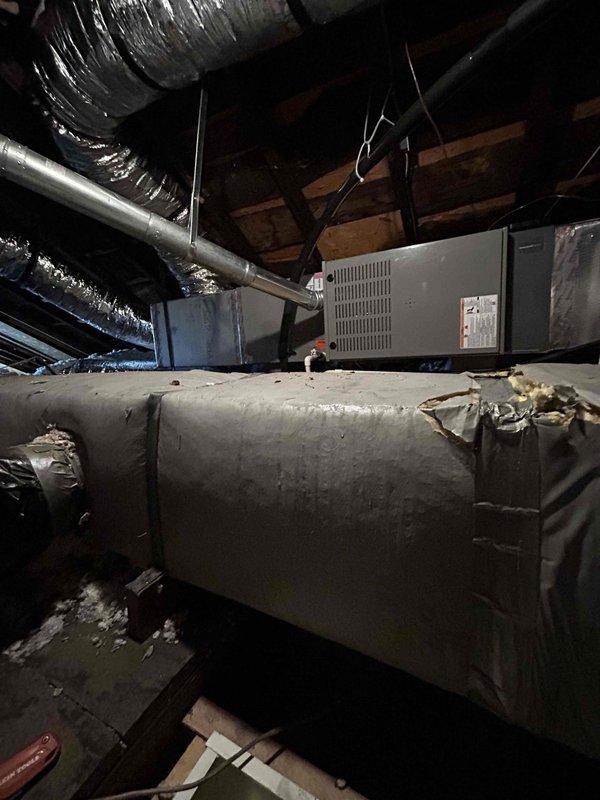 Responded to service call for thermostat unable to maintain set temperature of 72°F, with room remaining at 68°F. Upon arrival, accessed attic space to inspect HVAC system and air handler unit. Discovered significant deterioration of condensate drain pan with large crack running through center, causing structural failure and potential water drainage issues. Identified damaged and deteriorating duct insulation on primary supply duct with torn sections, frayed edges, and exposed underlying material compromising system efficiency. Documented all findings with photographs showing extent of damage to both drain pan and duct insulation. Advised that compromised drain pan poses risk of water damage and must be replaced, and damaged insulation is causing heat loss/gain affecting system's ability to maintain desired temperature. Recommended immediate replacement of cracked drain pan and re-insulation of damaged ductwork to restore proper system operation and temperature control.