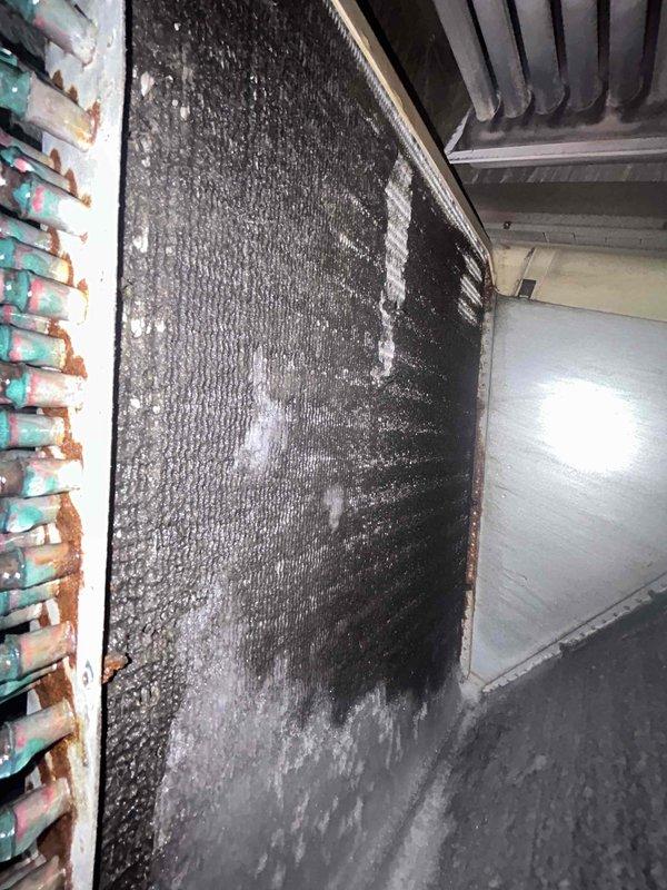 Responded to service call for 14-year-old AC unit not cooling with refrigerant line freezing, a recurring issue following recent repair. Upon inspection, discovered evaporator coil heavily clogged with dust and debris accumulation, severely restricting airflow and causing the freezing condition. Copper refrigerant tubing showed extensive corrosion with verdigris patina and rust staining at connection points. Aluminum fins on A-frame coil assembly were densely packed with dirt and contaminants. Documented equipment condition with photos showing significant lack of preventive maintenance. The restricted airflow from the dirty coil was the root cause of the freezing line issue. Recommended thorough coil cleaning and evaluation of refrigerant charge levels to restore proper system operation and prevent continued freezing problems.