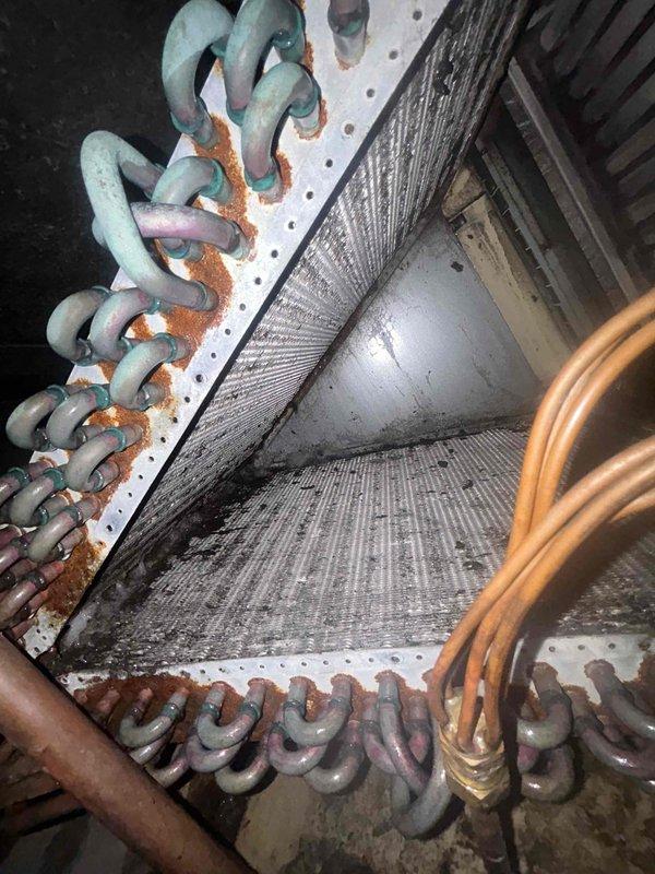 Responded to service call for 14-year-old AC unit not cooling with refrigerant line freezing, a recurring issue following recent repair. Upon inspection, discovered evaporator coil heavily clogged with dust and debris accumulation, severely restricting airflow and causing the freezing condition. Copper refrigerant tubing showed extensive corrosion with verdigris patina and rust staining at connection points. Aluminum fins on A-frame coil assembly were densely packed with dirt and contaminants. Documented equipment condition with photos showing significant lack of preventive maintenance. The restricted airflow from the dirty coil was the root cause of the freezing line issue. Recommended thorough coil cleaning and evaluation of refrigerant charge levels to restore proper system operation and prevent continued freezing problems.