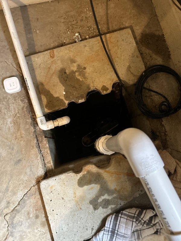 Responded to sump pump system disconnection in basement storage room. Upon arrival, found white PVC discharge pipe had been physically dislodged from main drainage line after accidental contact during storage activities. System had been unplugged as precautionary measure. 

Assessed water damage on surrounding tile and concrete flooring, noting significant staining and moisture accumulation around sump pit access point. Inspected all PVC piping connections and discharge line configuration. Reconnected and secured discharge pipe to main drainage line using appropriate fittings and primer/cement application. Verified proper pipe alignment and support to prevent future disconnection. Tested system operation by plugging unit back in and running through complete pump cycle. Confirmed proper water discharge through reconnected line with no leaks at connection points. Advised on importance of maintaining clearance around exposed piping to prevent accidental damage during storage activities.