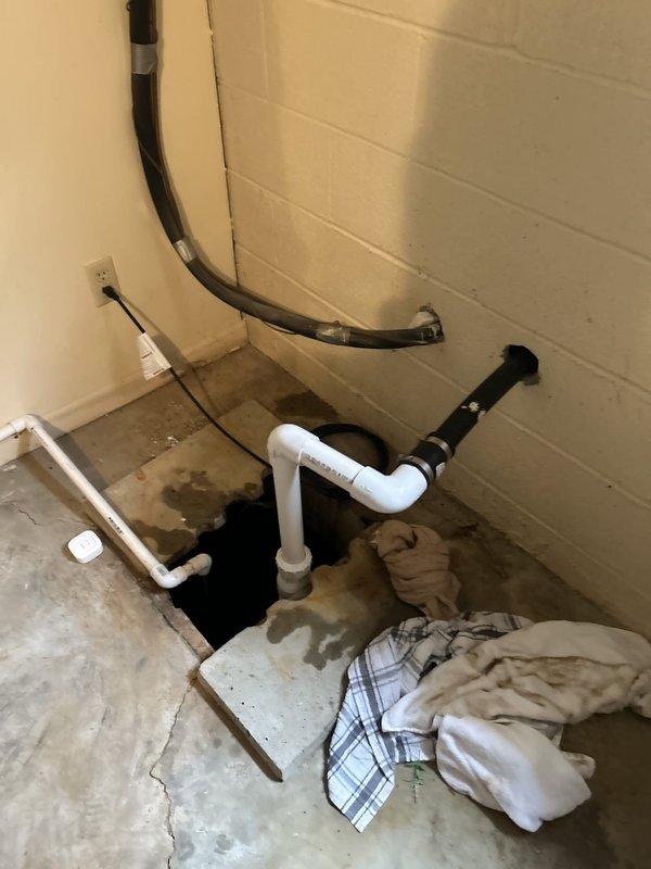 Responded to sump pump system disconnection in basement storage room. Upon arrival, found white PVC discharge pipe had been physically dislodged from main drainage line after accidental contact during storage activities. System had been unplugged as precautionary measure. 

Assessed water damage on surrounding tile and concrete flooring, noting significant staining and moisture accumulation around sump pit access point. Inspected all PVC piping connections and discharge line configuration. Reconnected and secured discharge pipe to main drainage line using appropriate fittings and primer/cement application. Verified proper pipe alignment and support to prevent future disconnection. Tested system operation by plugging unit back in and running through complete pump cycle. Confirmed proper water discharge through reconnected line with no leaks at connection points. Advised on importance of maintaining clearance around exposed piping to prevent accidental damage during storage activities.