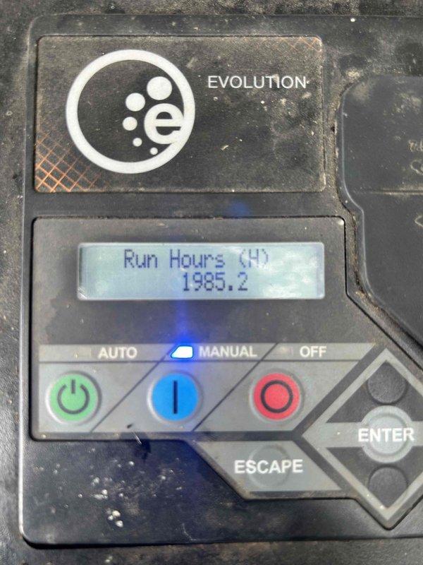 Responded to service call for Generac Evolution series generator that displayed a service message and would not start. Upon arrival, performed diagnostic inspection of the unit which showed 1985.2 run hours on the display. Assessed control panel functionality and verified all electrical connections at the generator. Inspected battery terminals and connections, noting the presence of battery cables with red and black insulation. Evaluated the control board interface showing AUTO, MANUAL, and OFF mode selections. Documented unit condition and operational status through photographs for service records.