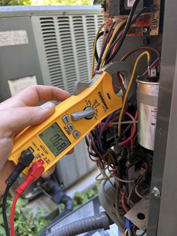 Responded to no cooling complaint on upstairs heat pump system with air handler located in attic. Upon arrival, performed diagnostic testing using multimeter to check electrical components including capacitor and control board connections. Measured voltage readings at 115V, indicating proper power supply to unit. Inspected condensate drain system and discovered wooden support beam positioned on drain pan with evidence of water staining and potential drainage issues. Identified compromised drain pan integrity with visible corrosion around wooden support structure. Cleared obstruction from drain line where PVC piping and insulation were improperly configured. System restored to proper cooling operation after addressing drainage concerns and verifying all electrical components functioning within normal parameters.