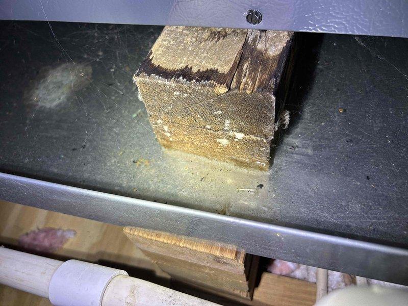 Responded to no cooling complaint on upstairs heat pump system with air handler located in attic. Upon arrival, performed diagnostic testing using multimeter to check electrical components including capacitor and control board connections. Measured voltage readings at 115V, indicating proper power supply to unit. Inspected condensate drain system and discovered wooden support beam positioned on drain pan with evidence of water staining and potential drainage issues. Identified compromised drain pan integrity with visible corrosion around wooden support structure. Cleared obstruction from drain line where PVC piping and insulation were improperly configured. System restored to proper cooling operation after addressing drainage concerns and verifying all electrical components functioning within normal parameters.