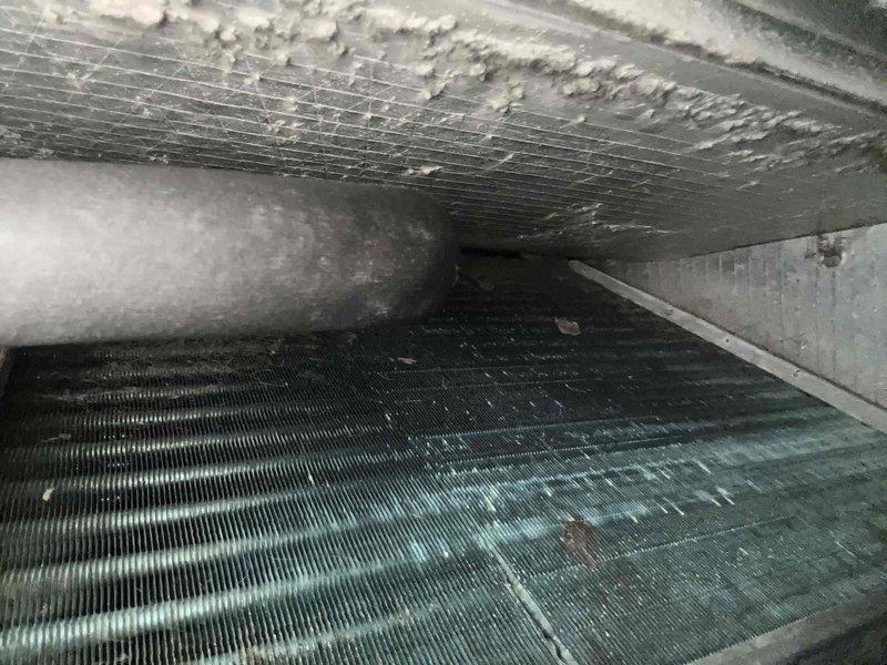 # HVAC Visual Inspection - AC and Furnace System

Performed comprehensive visual inspection of residential HVAC system including approximately 17-year-old air conditioning unit and furnace per customer request. Indoor air handler located in crawlspace.

## Findings

**Evaporator Coil:** Inspected indoor coil assembly and discovered heavy dust and debris accumulation on coil fins, significantly restricting airflow. Observed extensive ice formation and frost buildup on upper plenum surfaces, indicating restricted airflow and potential refrigerant issues. Coil fins heavily soiled with grayish-black contamination throughout.

**System Performance Issues:** Ice accumulation on coil components suggests system is operating under conditions causing abnormal moisture freezing, likely due to combination of reduced airflow from dirty coils and possible low refrigerant charge. This condition will severely impact cooling efficiency and system capacity.

**Water Heater (Incidental Observation):** No