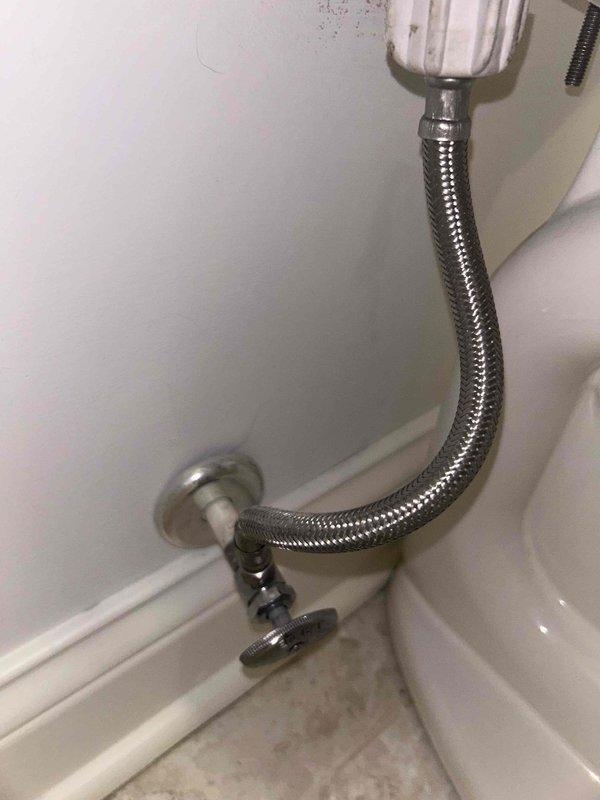 Responded to complaint of whistling shut-off valve behind toilet. Inspected wall-mounted chrome shut-off valve and flexible braided stainless steel supply line connecting to toilet tank. Valve was producing audible whistling noise but showed no visible water leakage at time of inspection. Examined supply line connections at both wall valve and tank inlet, noting standard installation with proper coupling. Multiple toilets present in home but issue isolated to single fixture.