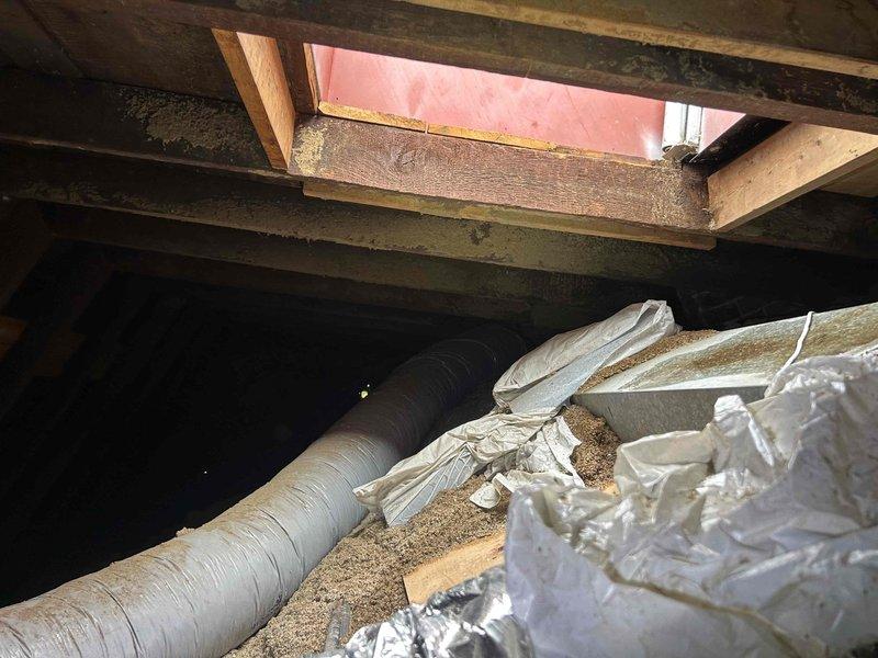 Responded to callback for water leak originating from roof hatch access point following recent maintenance service. Upon inspection, identified active water intrusion at hatch opening leading to attic space where HVAC equipment is accessed. Documented visible water damage on interior ceiling below hatch location, including brown discoloration and staining on drywall surface near track lighting fixtures. Photographed attic access area showing hatch framing, exposed structural beams with moisture staining, HVAC ductwork, and insulation materials. Confirmed leak was not present prior to maintenance visit, indicating potential weather seal compromise or hatch closure issue during service access. Recommended immediate weatherproofing repair to hatch assembly and monitoring of affected ceiling area for additional moisture damage.