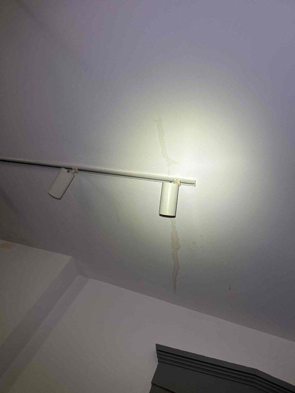 Responded to callback for water leak originating from roof hatch access point following recent maintenance service. Upon inspection, identified active water intrusion at hatch opening leading to attic space where HVAC equipment is accessed. Documented visible water damage on interior ceiling below hatch location, including brown discoloration and staining on drywall surface near track lighting fixtures. Photographed attic access area showing hatch framing, exposed structural beams with moisture staining, HVAC ductwork, and insulation materials. Confirmed leak was not present prior to maintenance visit, indicating potential weather seal compromise or hatch closure issue during service access. Recommended immediate weatherproofing repair to hatch assembly and monitoring of affected ceiling area for additional moisture damage.